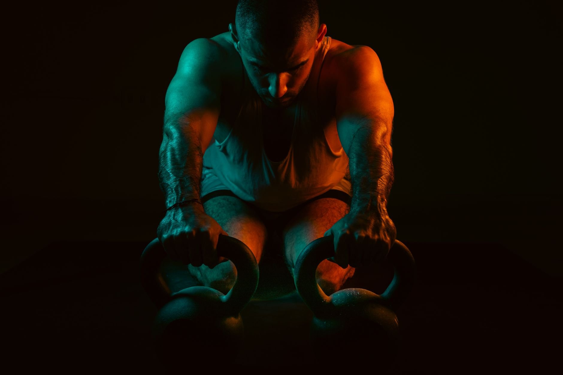 A strong man intensely working out with kettlebells in a dark gym setting.